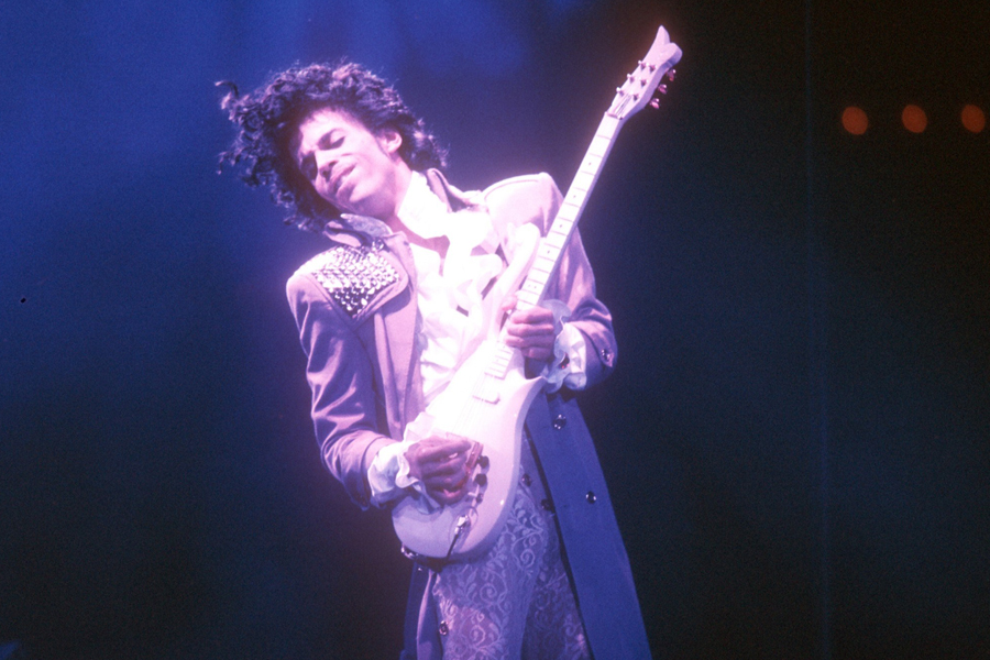 Prince playing guitar in purple light.