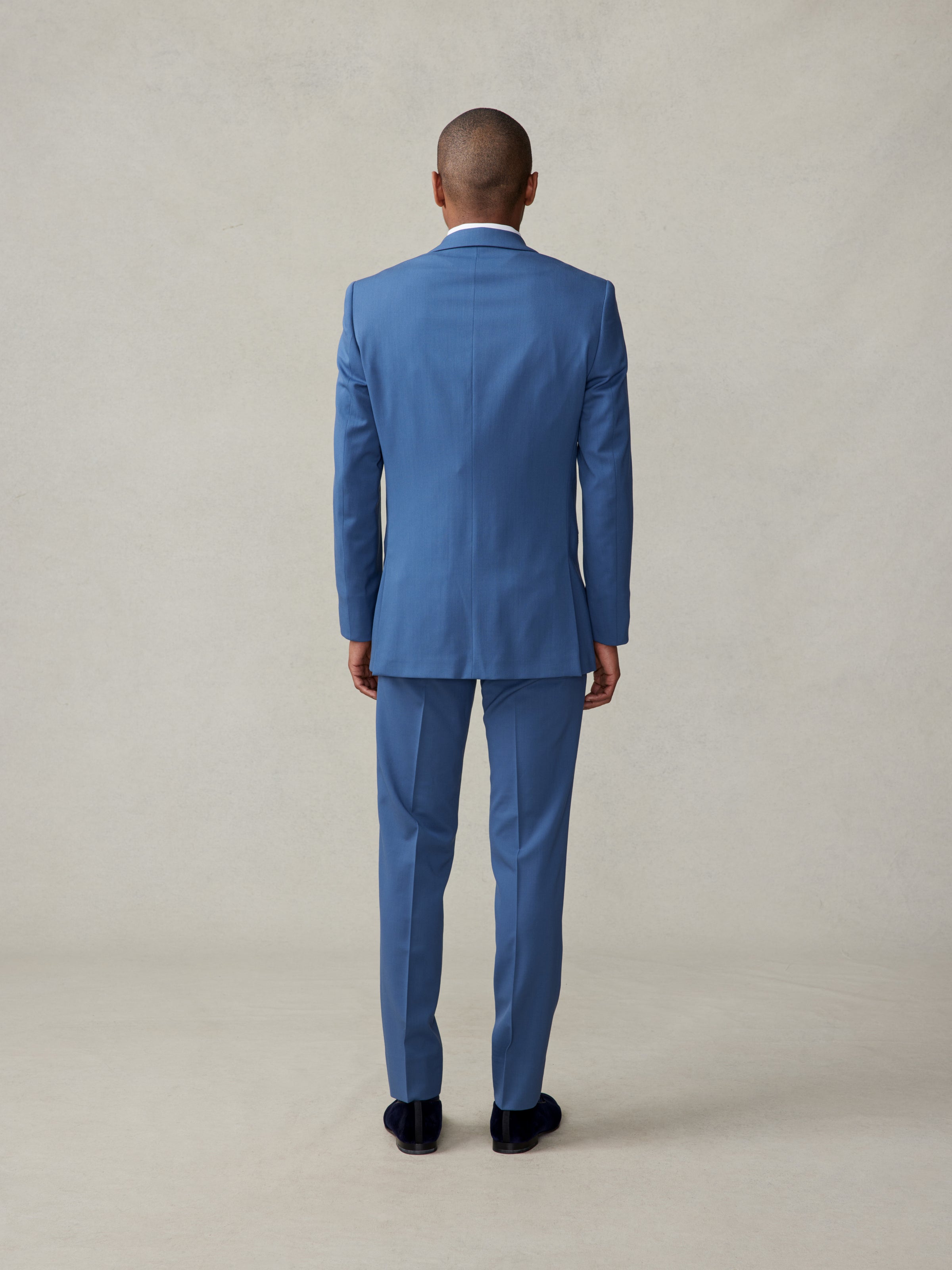 Man in a blue suit viewed from the back, standing on a neutral background.