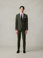 Man wearing a green suit, pink shirt, and black tie, standing against a neutral background.