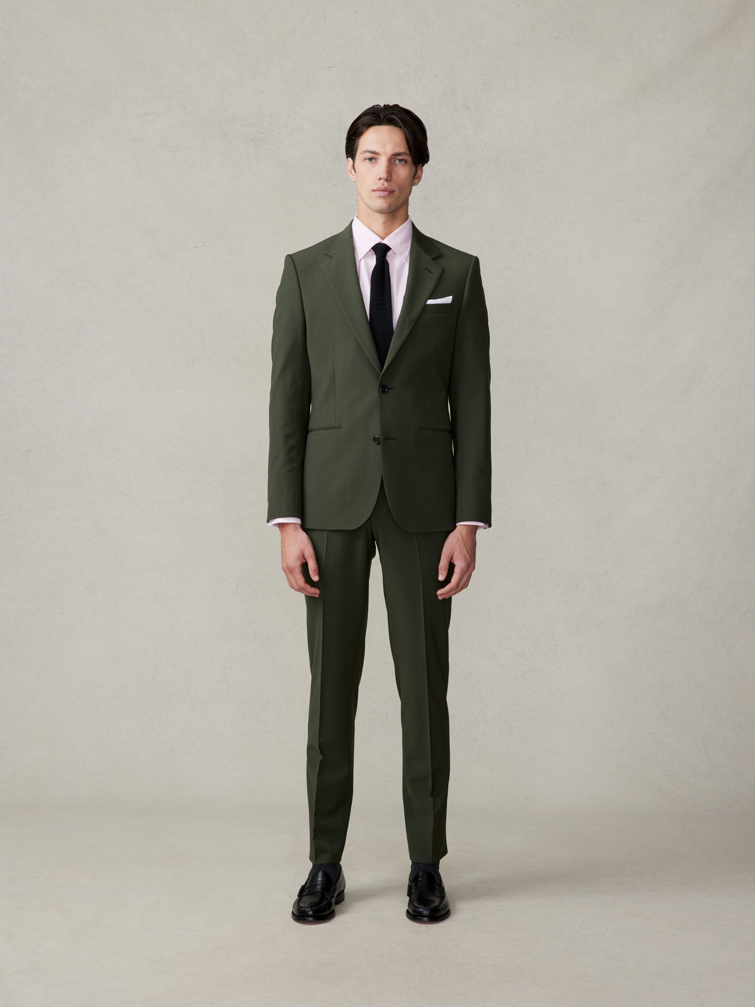 Man wearing a green suit, pink shirt, and black tie, standing against a neutral background.