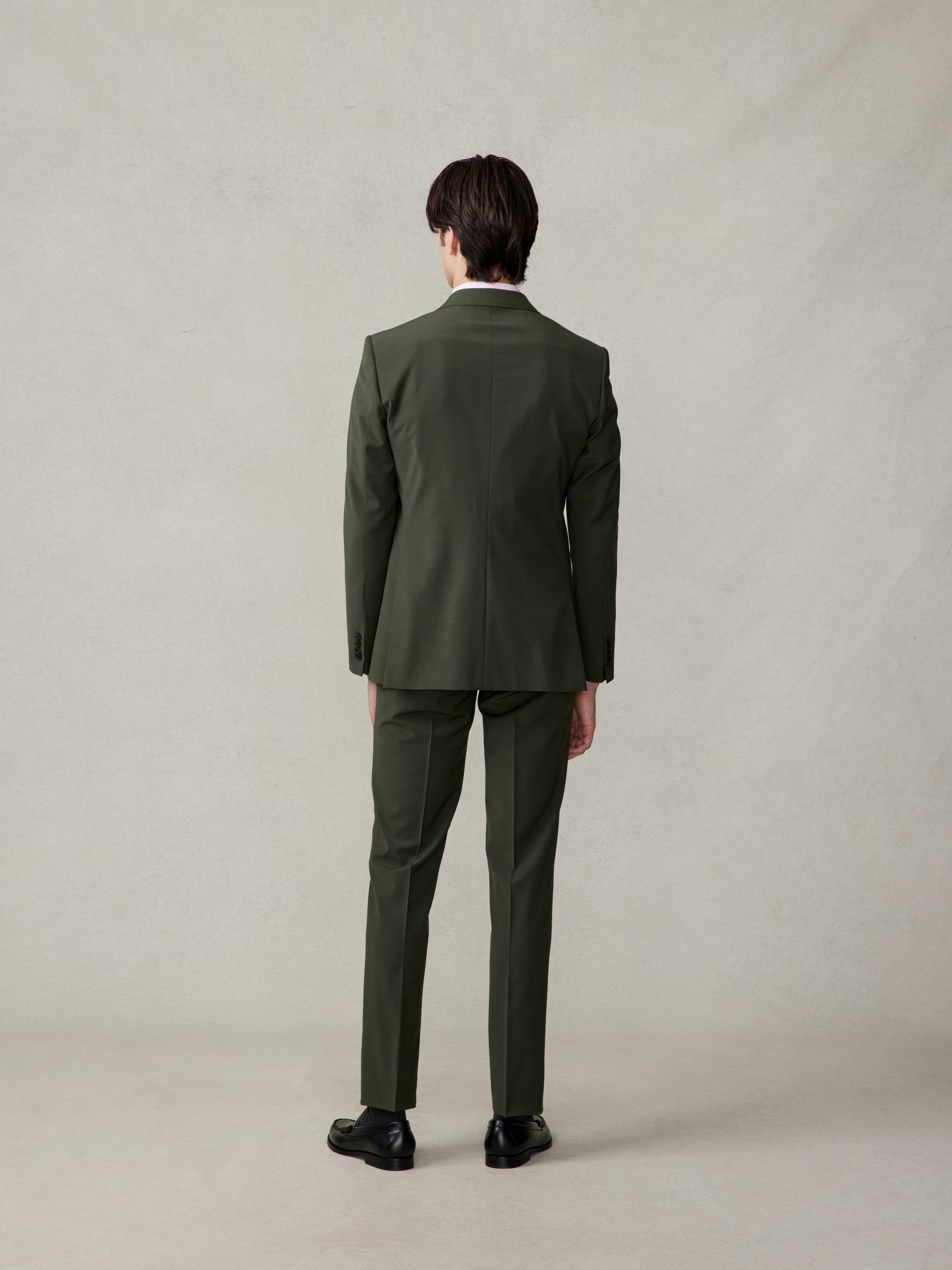 Man wearing a green suit, viewed from the back, standing on a neutral background.