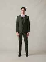 Man wearing a green suit with a pink shirt and black tie, standing against a neutral background.