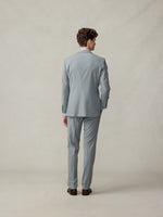 Man in a light grey suit viewed from the back, standing on a neutral background.