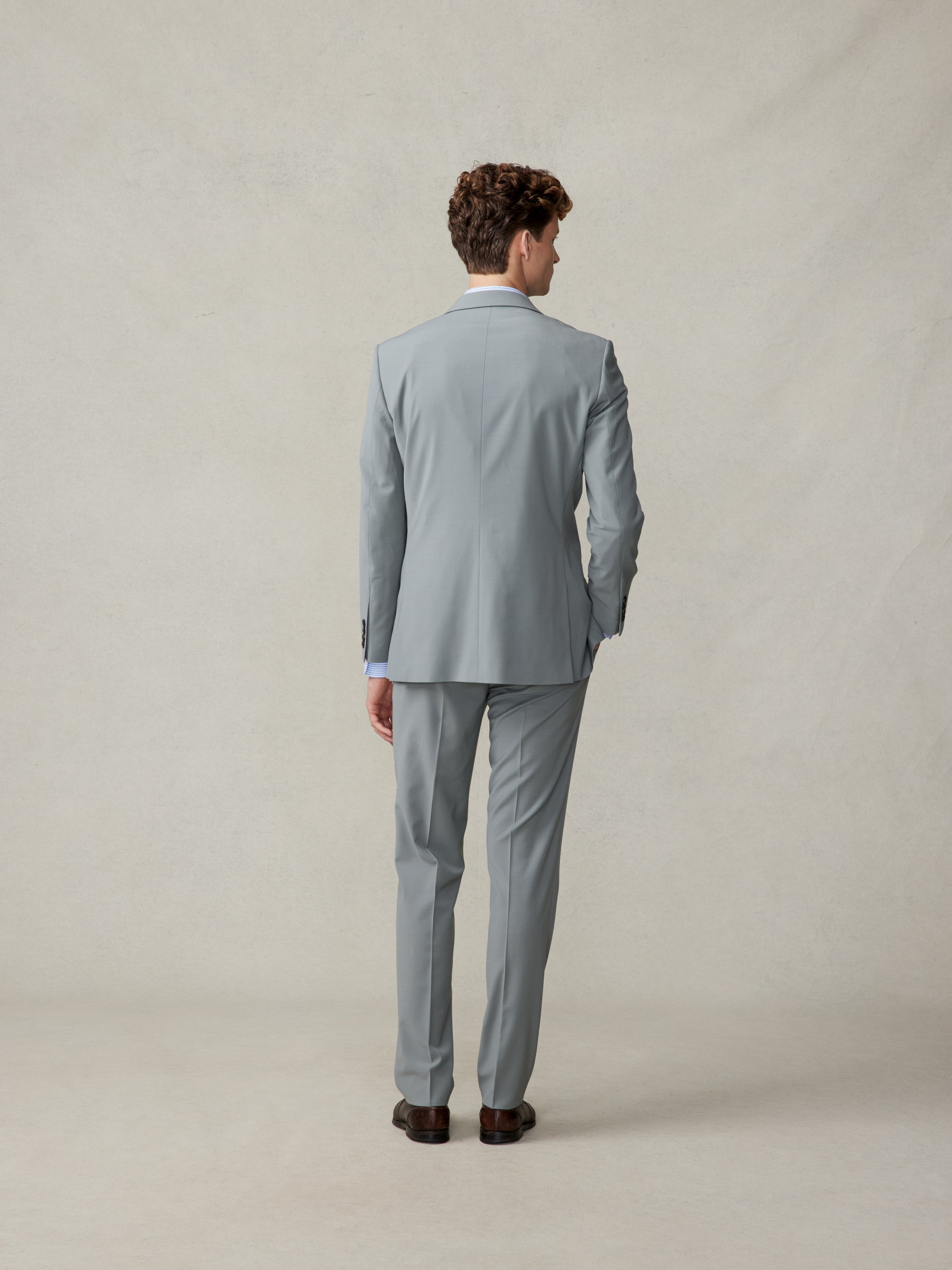 Man in a light grey suit viewed from the back, standing on a neutral background.
