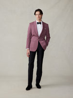 Man wearing a pink tuxedo jacket, black pants, and bow tie, standing against a neutral background.