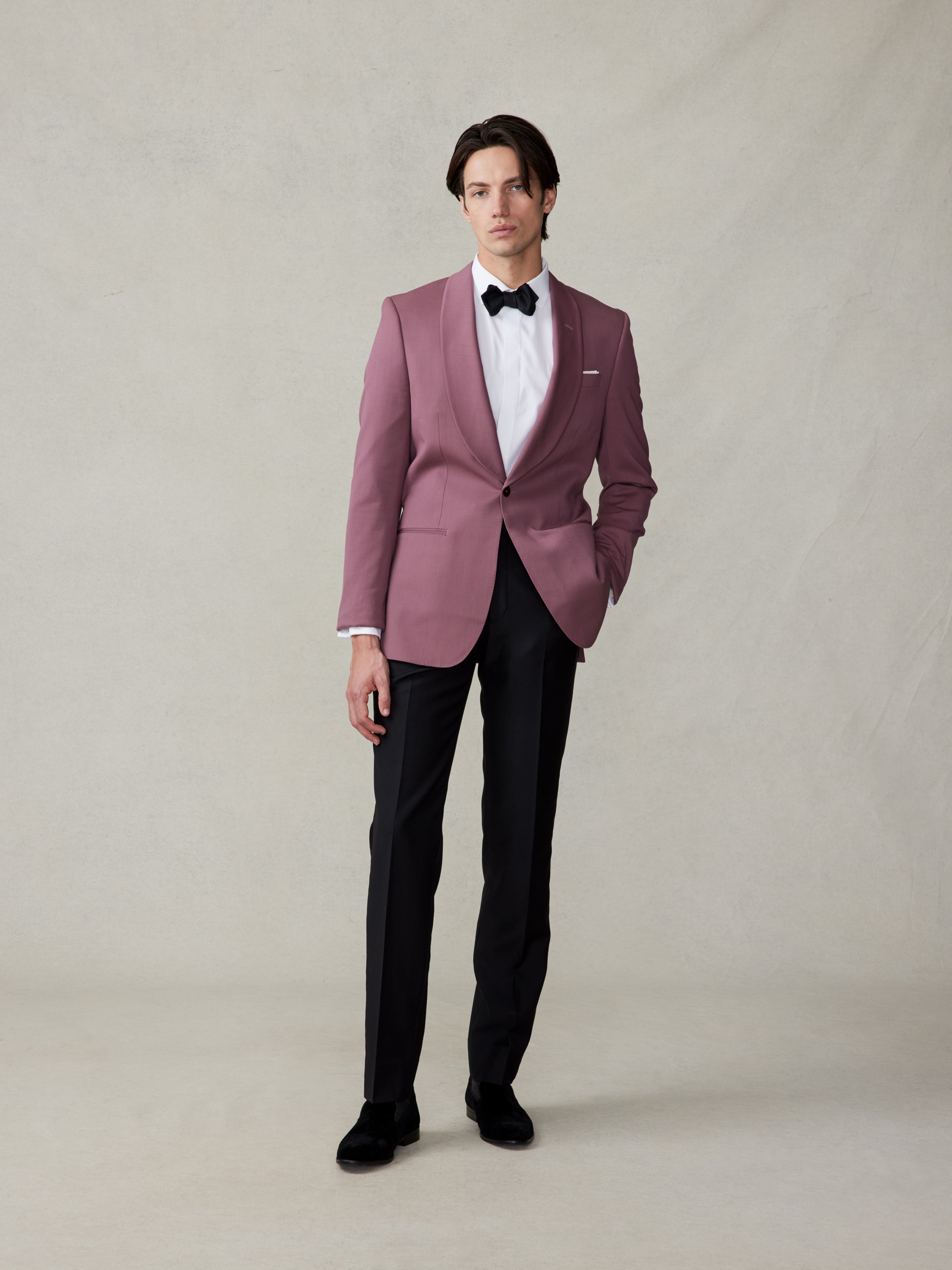 Man wearing a pink tuxedo jacket, black pants, and bow tie, standing against a neutral background.