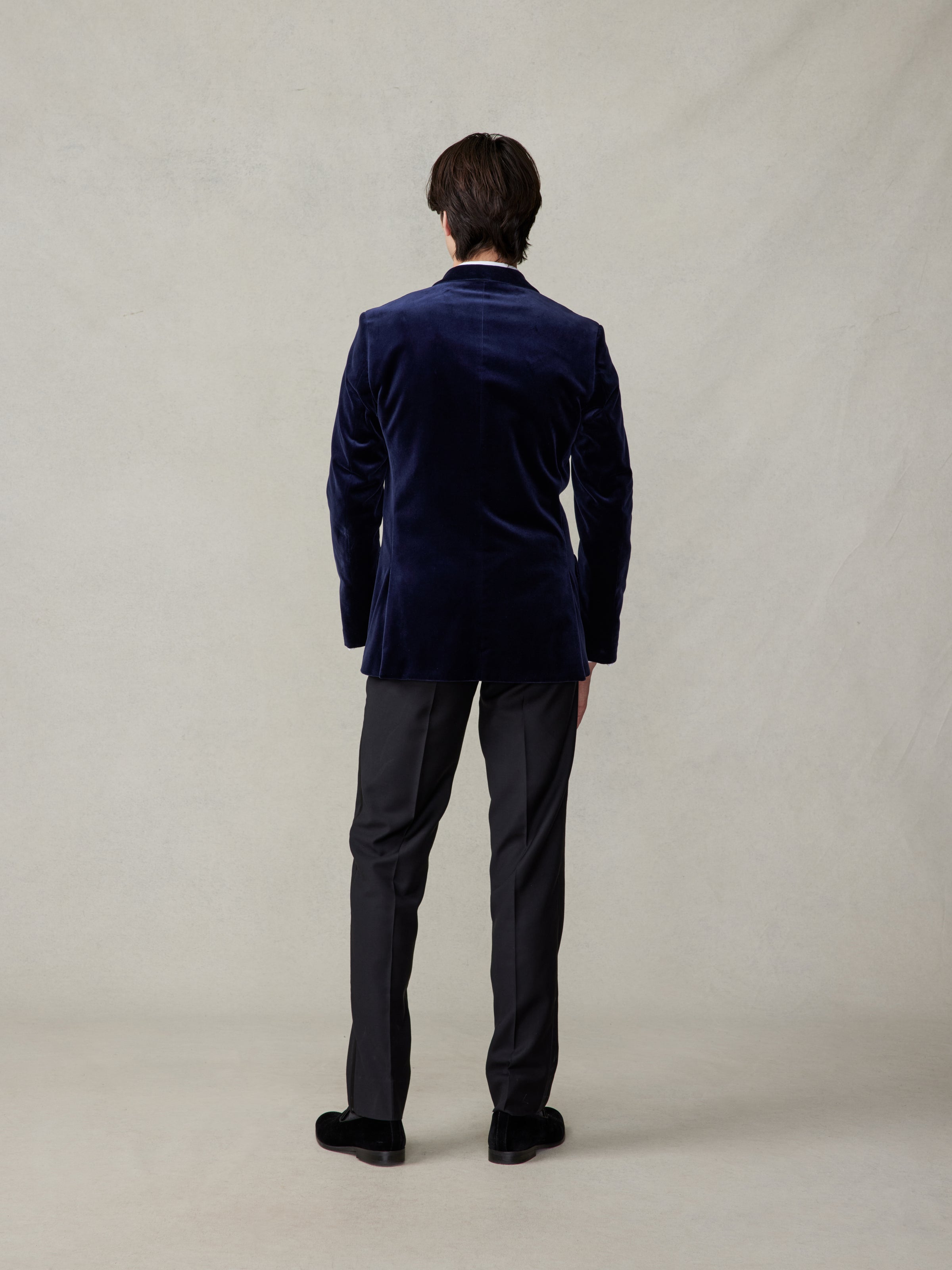 Back view of a man in an ocean blue velvet tuxedo jacket with black tuxedo pants.