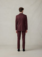 Man in a burgundy suit viewed from the back, standing against a neutral background.