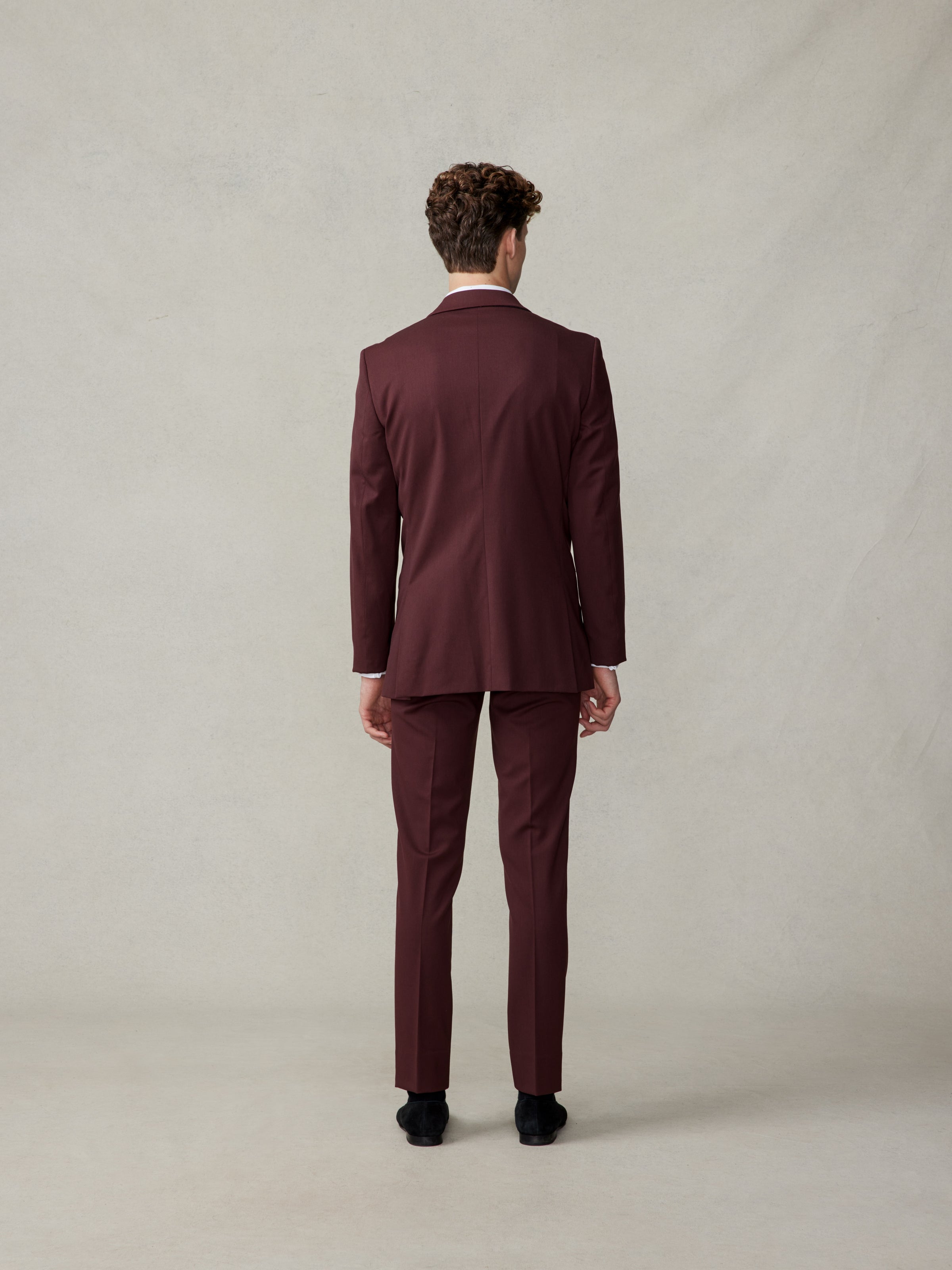 Man in a burgundy suit viewed from the back, standing against a neutral background.