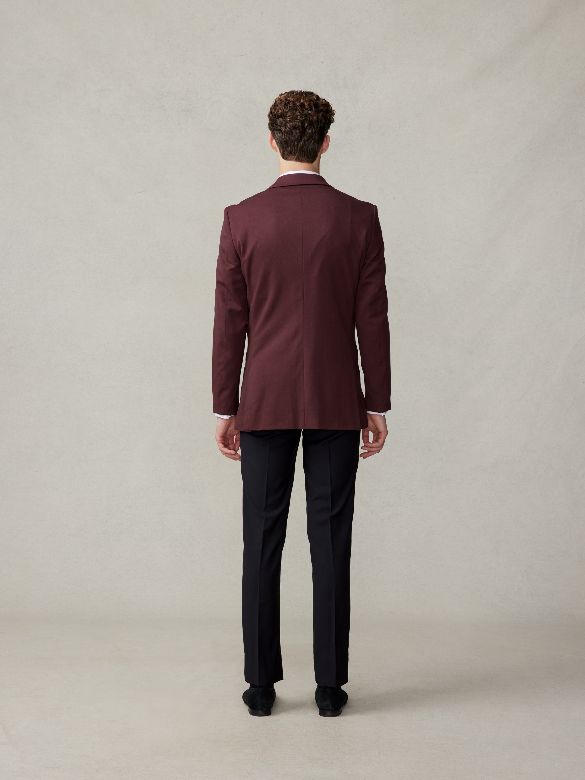 Man wearing a maroon suit jacket and black trousers, viewed from the back.