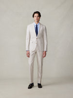 Man wearing a light beige suit with a blue tie and black shoes.