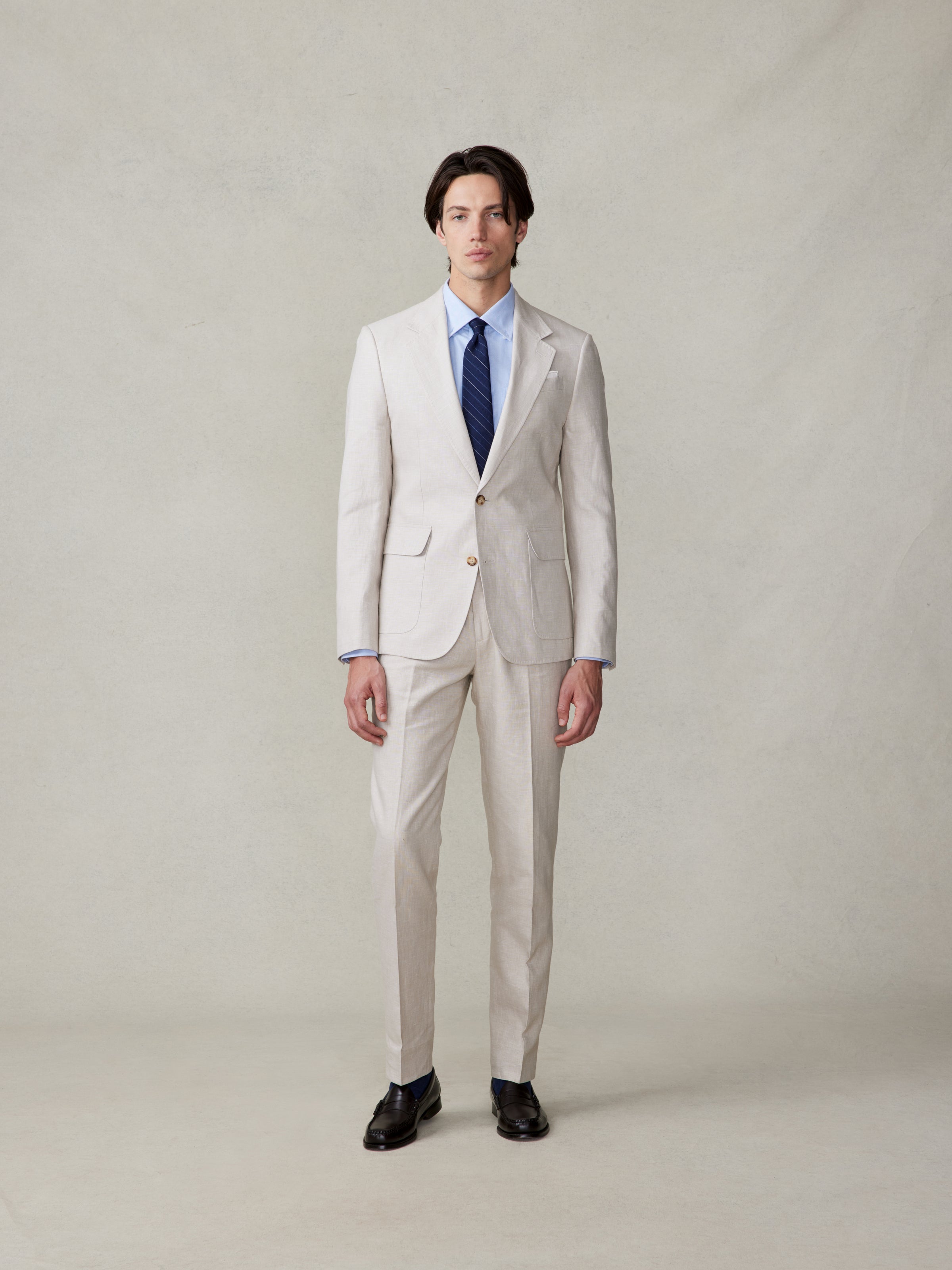 Man wearing a light beige suit with a blue tie and black shoes.