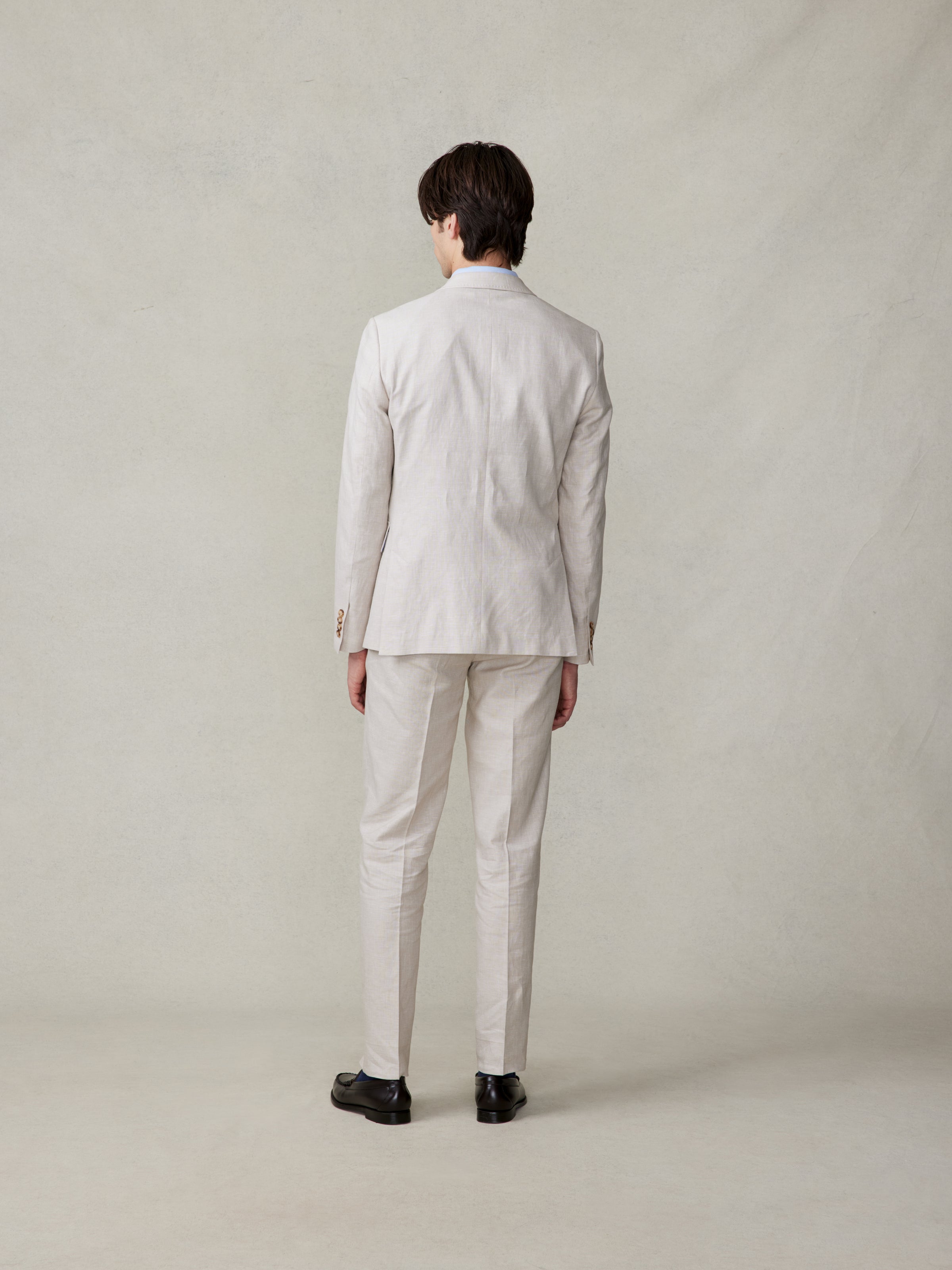 Man in a light-colored suit standing with his back to the camera.