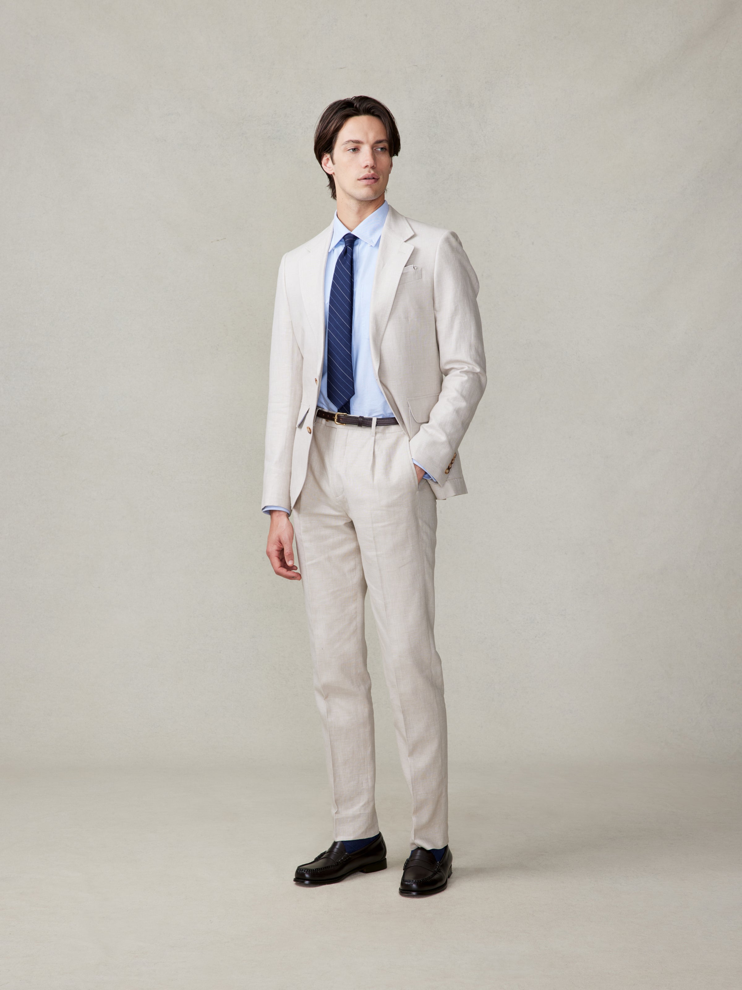 Man in a light beige suit with a blue shirt and tie, standing against a neutral background.