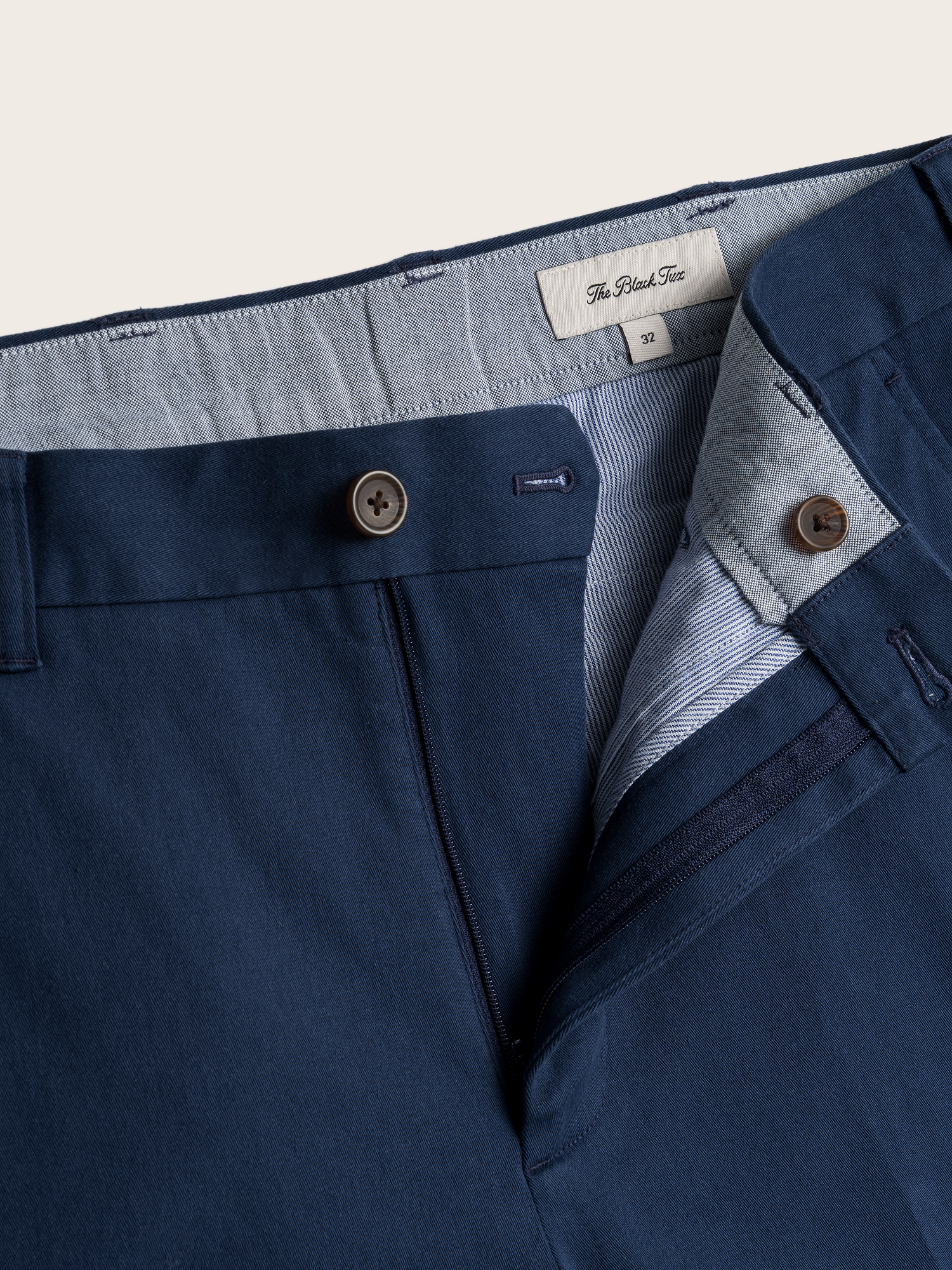 Close-up of navy chino pants waistband, button fly, and brand label