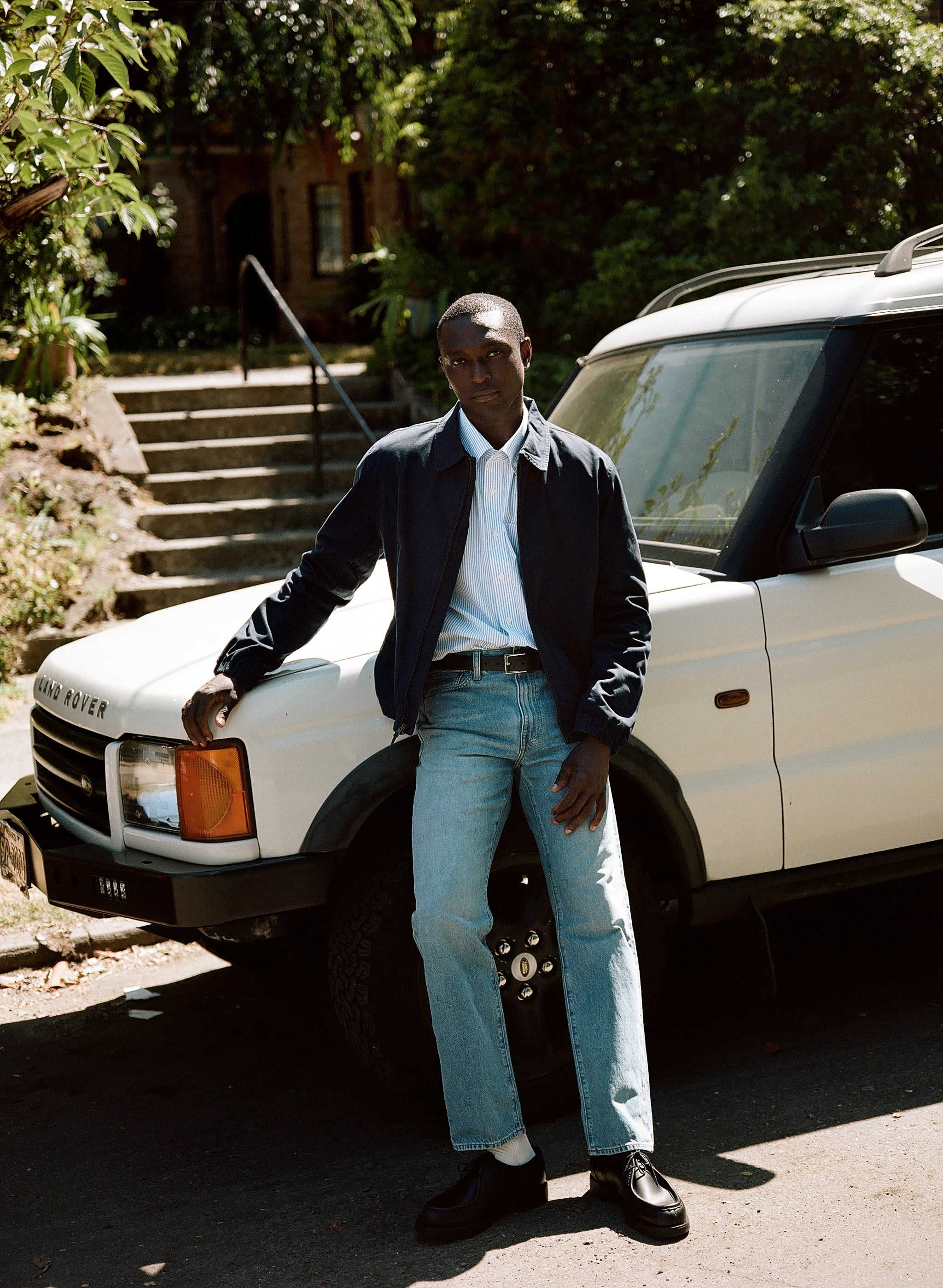 A person stands next to a white Land Rover, wearing a navy jacket and light blue jeans.