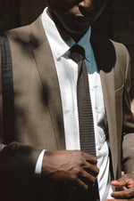 Person adjusting a black tie while wearing a brown suit and white shirt.