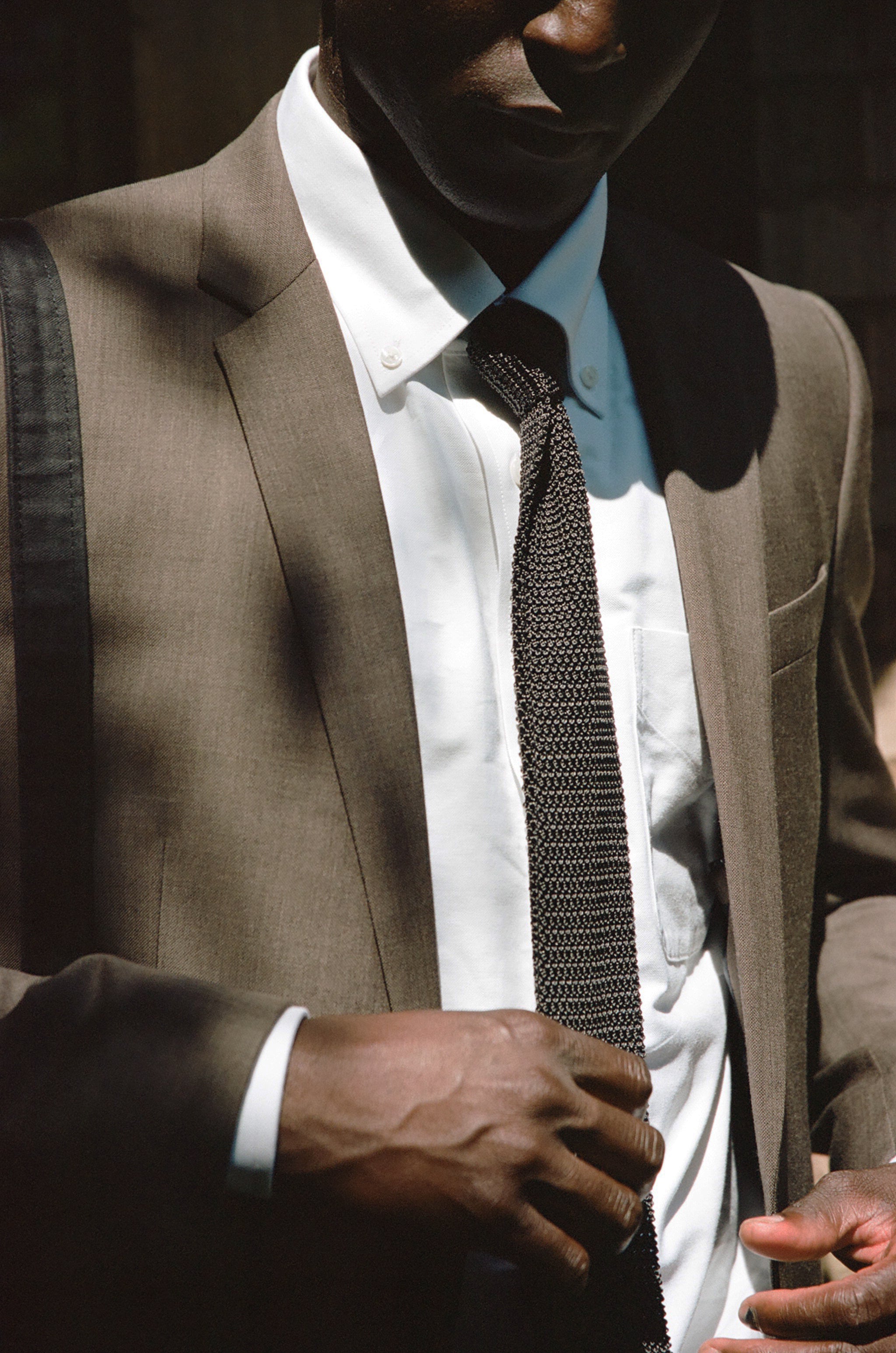 Person adjusting a black tie while wearing a brown suit and white shirt.