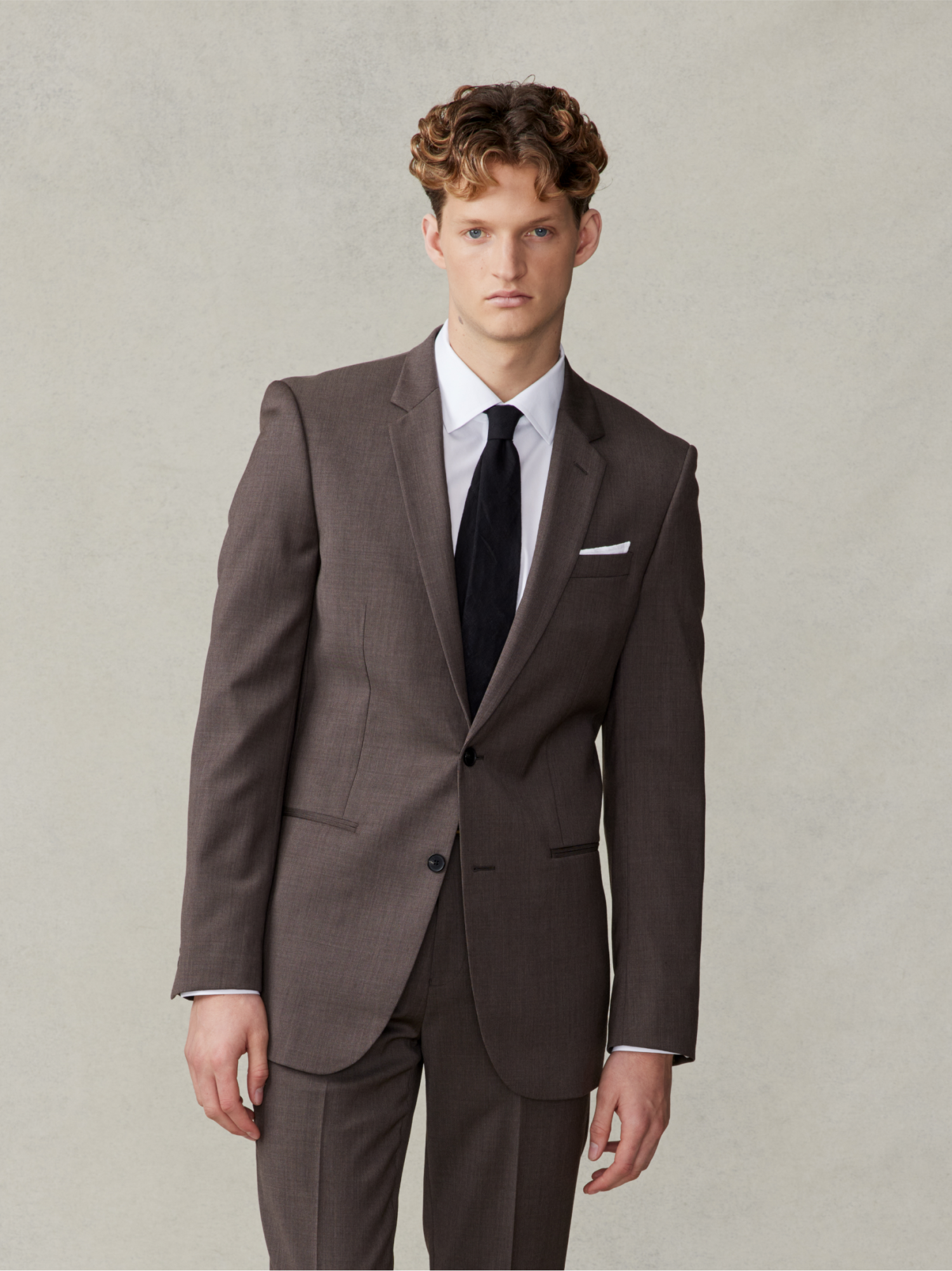 Man wearing a brown suit with a white shirt and black tie.