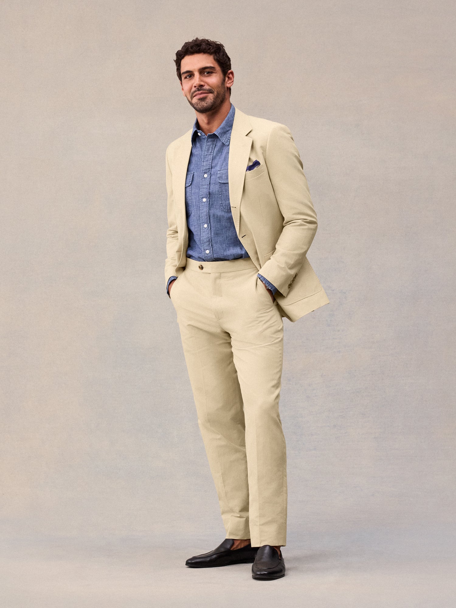 Editorial shot of harvest tan suit jacket worn open over a chambray shirt, hands in pockets