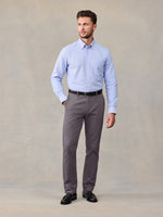 Man in a light blue button-down shirt and grey chino pants, standing against a tan backdrop.