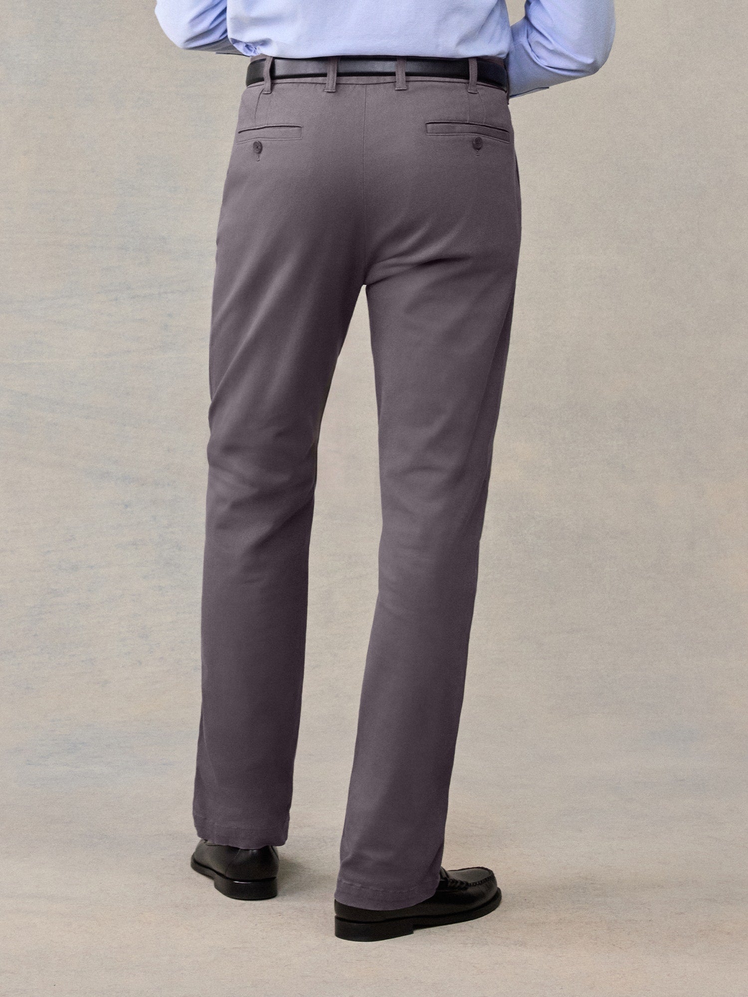 Back view of a man from waist down wearing grey chino pants with black belt and loafers.