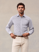 A man in a white and navy wide stripe dress shirt tucked into cream trousers with a brown belt, front view.