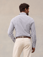 Back view of a man in a white and navy wide stripe dress shirt, cream trousers and brown belt, beige backdrop.