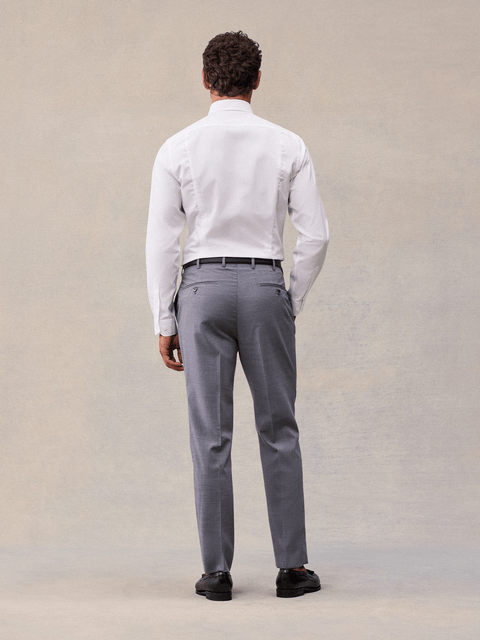 Back view of a man in slate grey suit trousers and a white dress shirt, full length, black loafers.