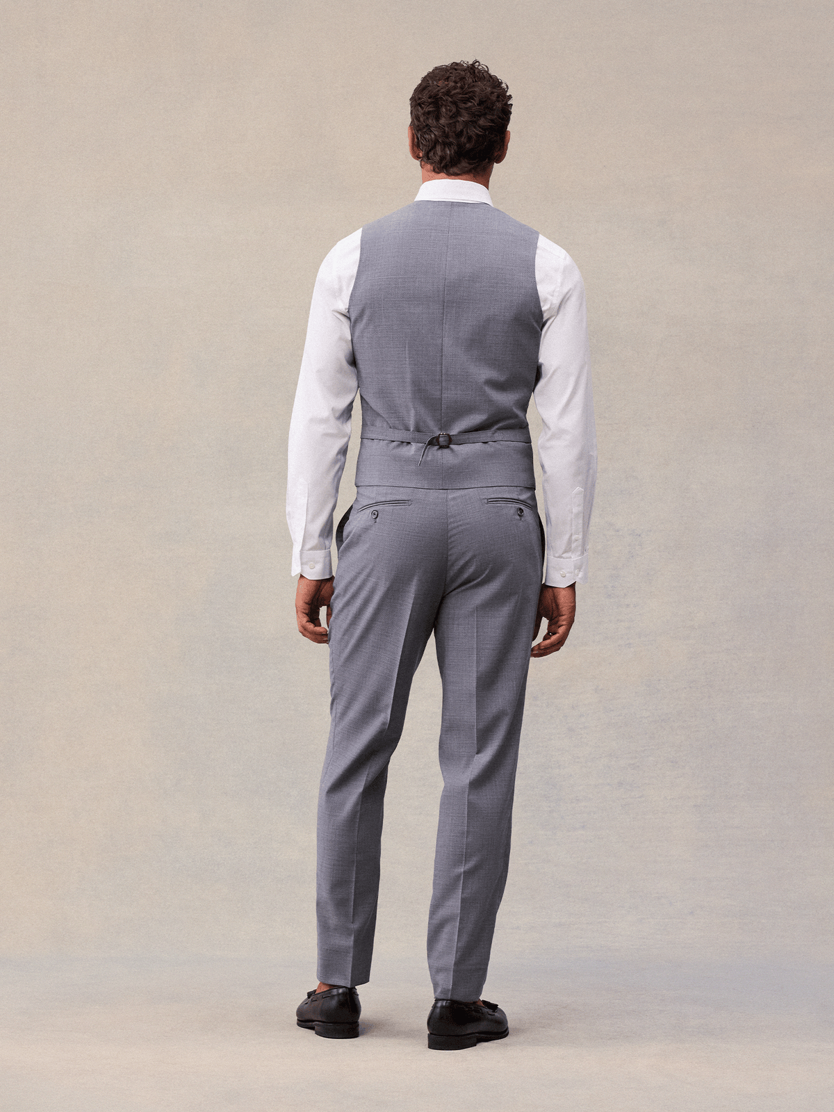 Back view of a man in a slate grey suit vest with adjustable back strap and matching trousers.
