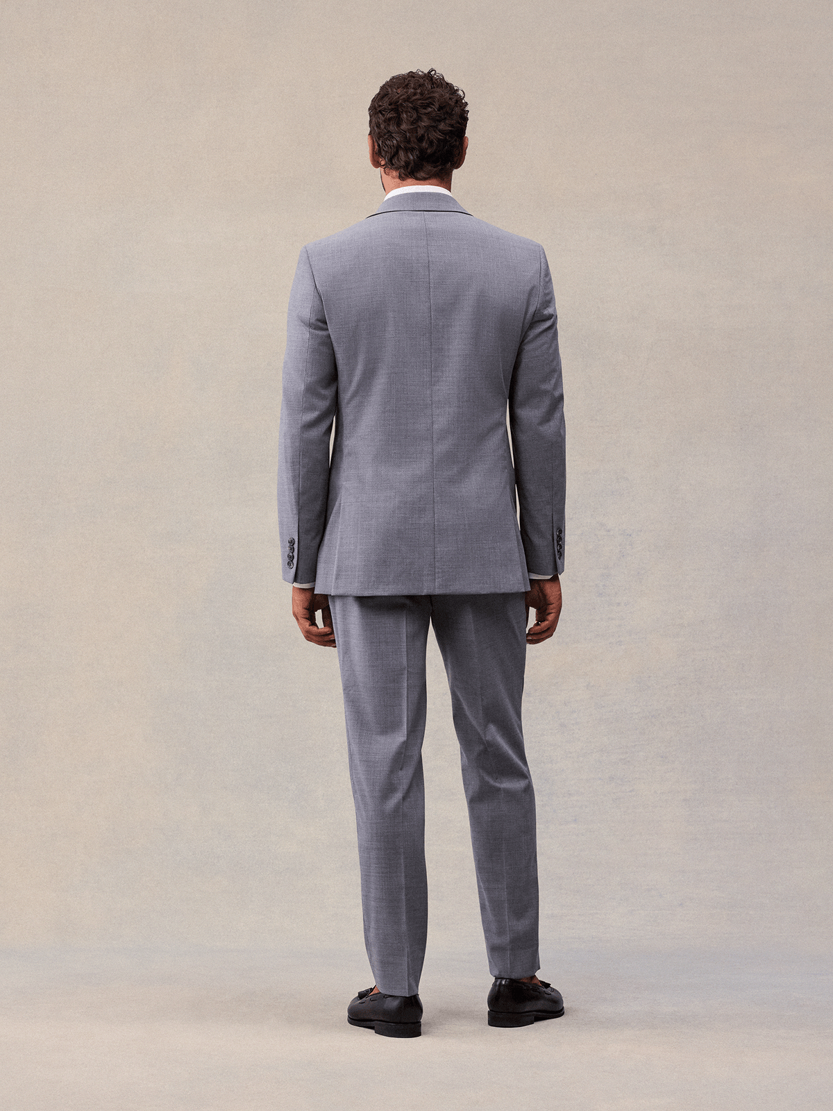 Back view of a man in a slate grey suit jacket and matching trousers, full length, black loafers.