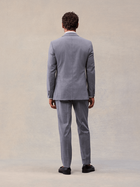 Back view of a man in a slate grey suit jacket and matching trousers, full length, black loafers.