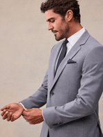 Close-up of a man adjusting his cuff in a slate grey stretch wool suit jacket, notch lapel and navy pindot tie.