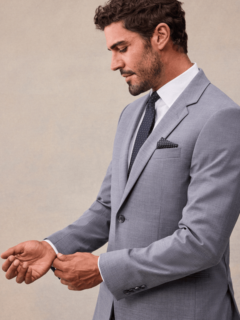 Close-up of a man adjusting his cuff in a slate grey stretch wool suit jacket, notch lapel and navy pindot tie.