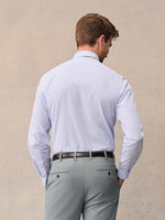 Back view of a man in a blue windowpane check dress shirt tucked into light grey trousers with a brown belt, beige backdrop.