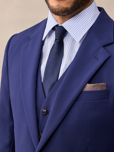 Close-up of a cove blue suit jacket notch lapel and vest, light blue check shirt, navy tie, brown pocket square.