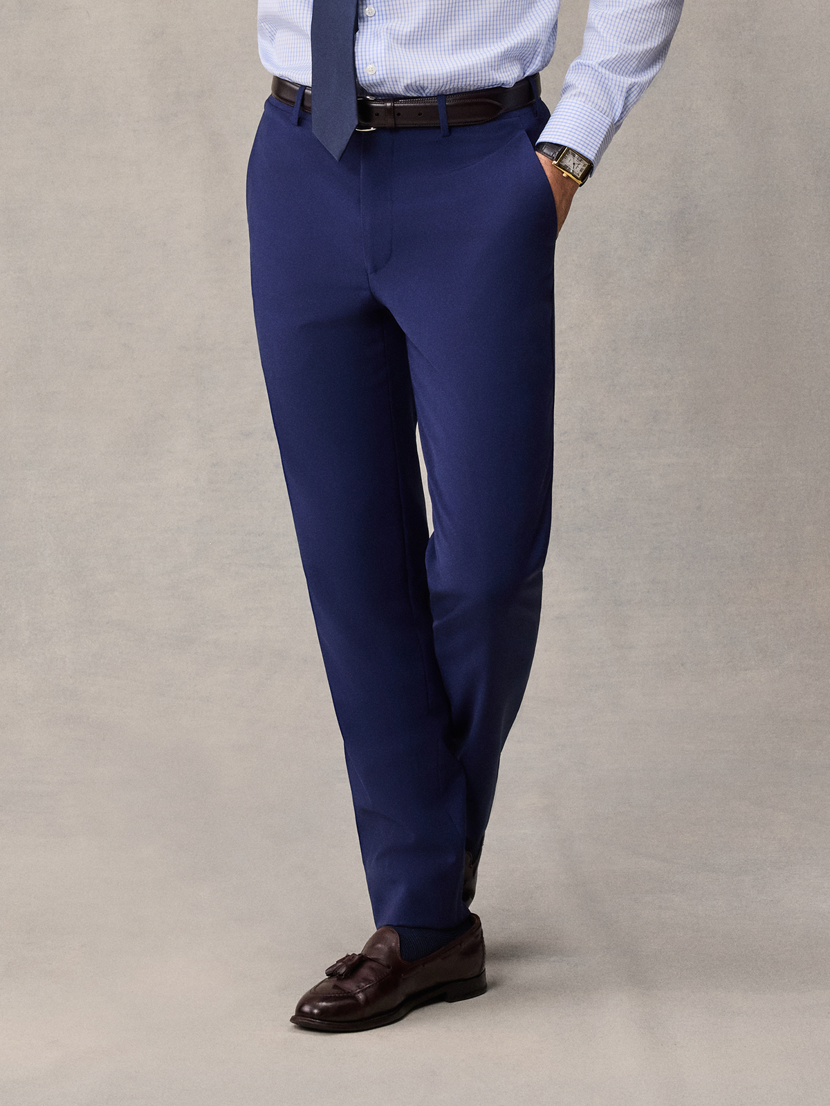 Cropped front view of cove blue suit pants with a light blue shirt, brown belt and tassel loafers.