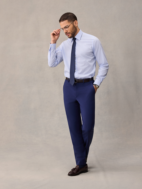 A man in cove blue suit pants, light blue dress shirt and navy tie, adjusting his glasses, full length.