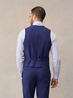 Back view of a cove blue suit vest with adjustable back strap, light blue shirt, cropped.