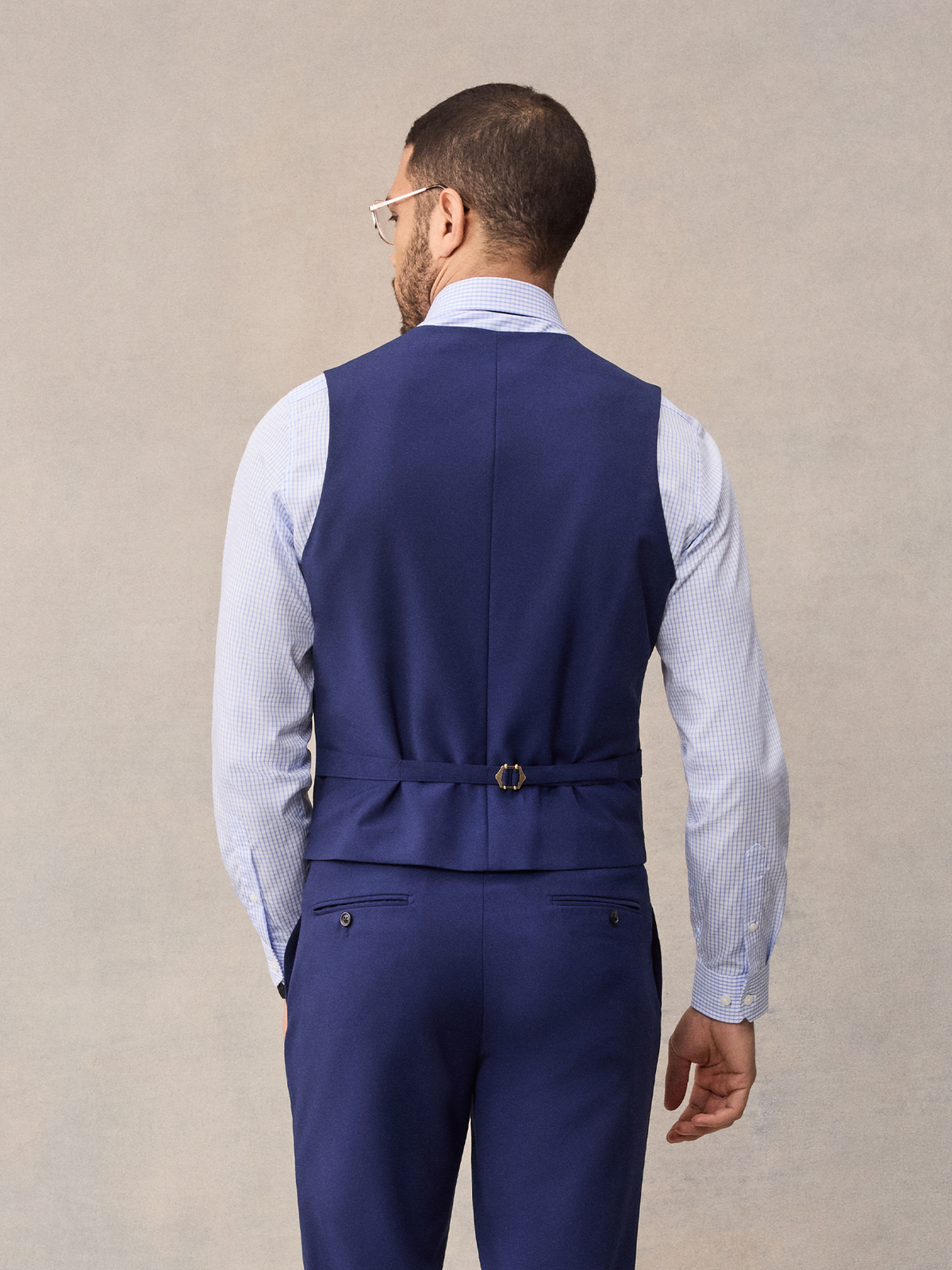 Back view of a cove blue suit vest with adjustable back strap, light blue shirt, cropped.