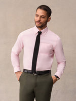 Man in pink oxford shirt and olive trousers with black knit tie, hands in pockets