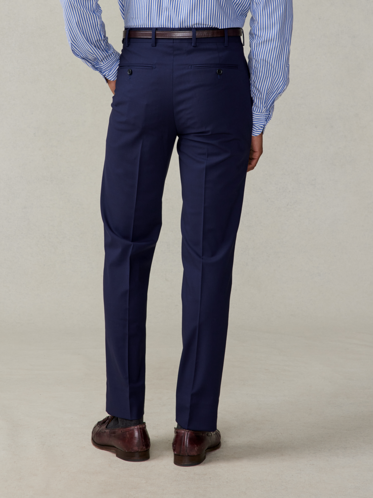 Back view of a person wearing navy dress pants and brown shoes.