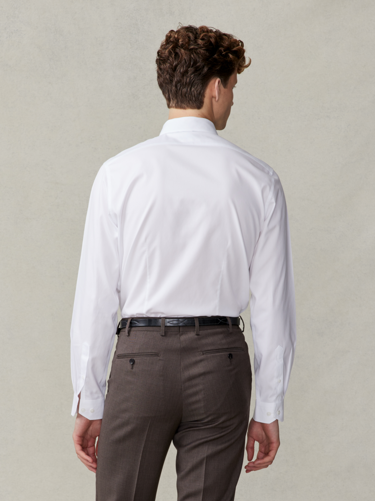 Man wearing a white shirt and brown trousers, viewed from the back.