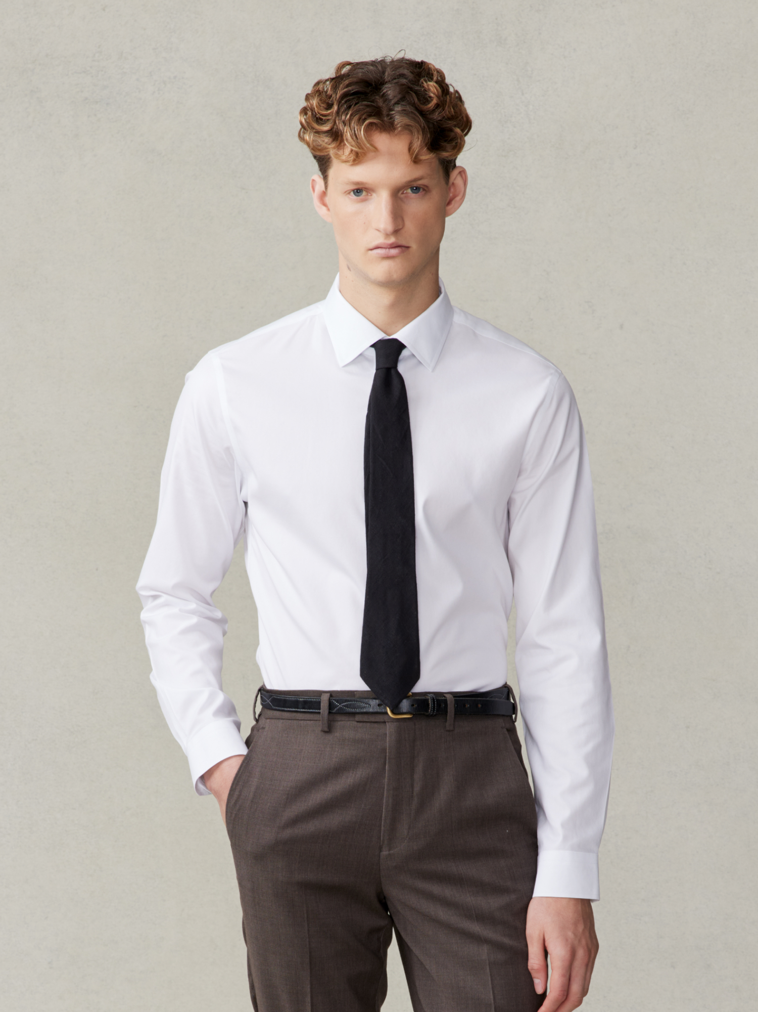 Man wearing a white shirt and black tie with brown trousers.