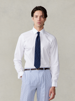 Man wearing a white shirt and navy tie with polka dots, standing against a light background.