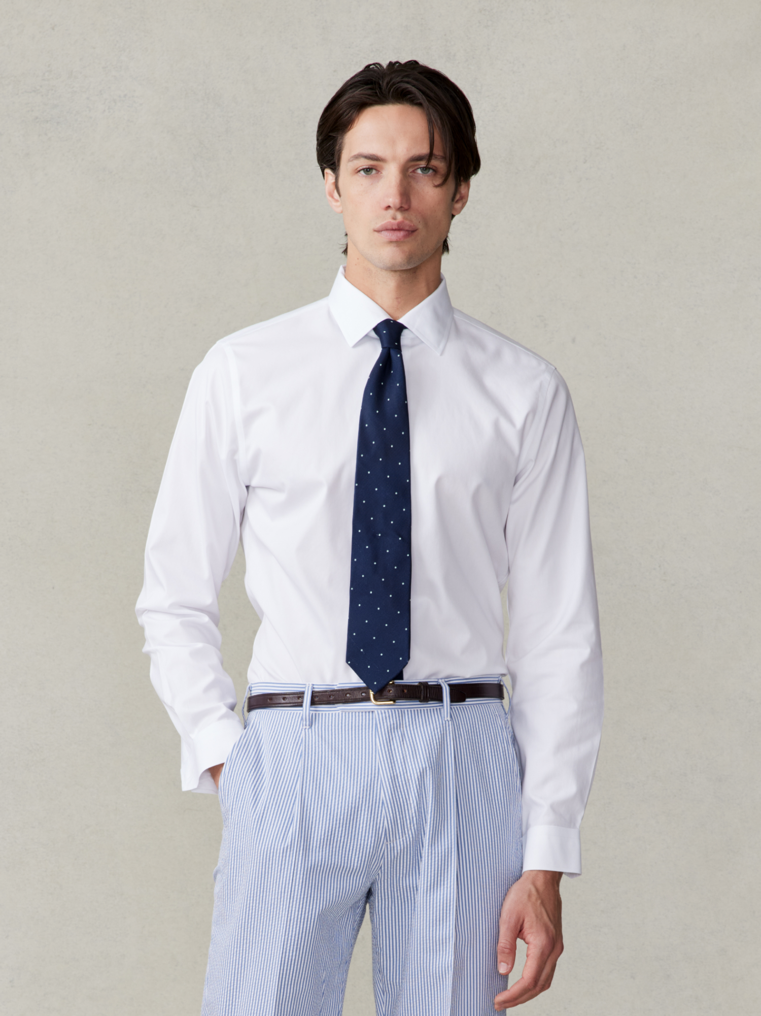 Man wearing a white shirt and navy tie with polka dots, standing against a light background.