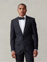 Man wearing a black tuxedo with a bow tie, standing against a neutral background.