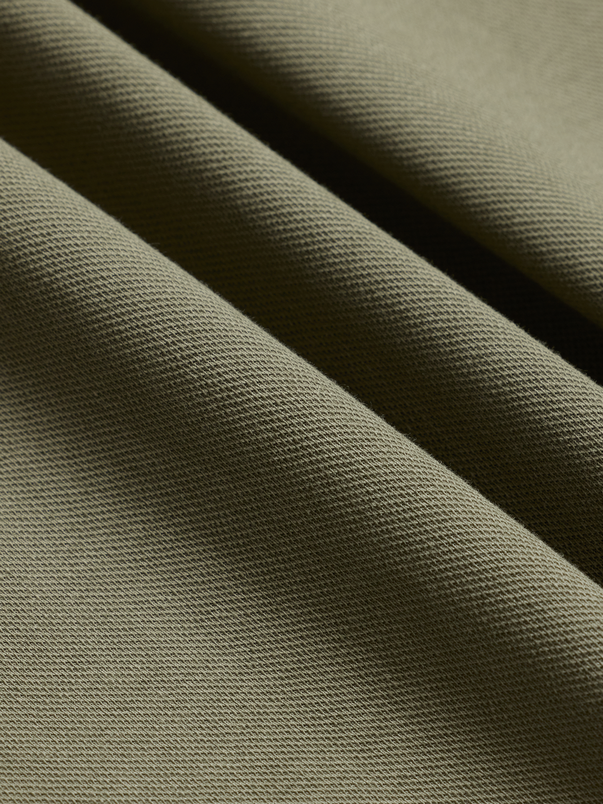 Close-up of olive green pique polo fabric texture, diagonal folds