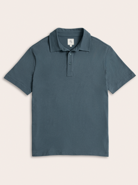 Slate blue pique polo shirt laid flat, front view, on cream background