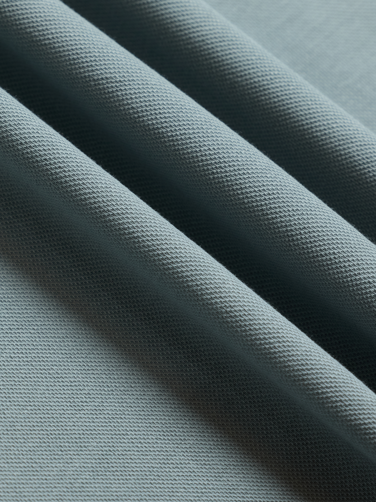Close-up of light blue polo shirt fabric with folds, showing pique knit texture